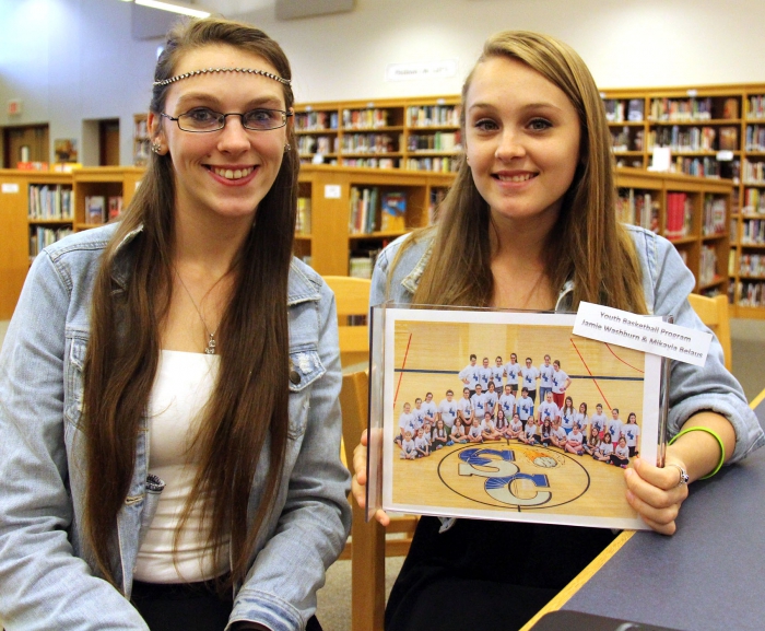Seniors Jamie Washburn, left, and Mikayla Belaus with a group photo of the girls' youth basketball program they organized for their senior English 20% project at Sandy Creek High School.