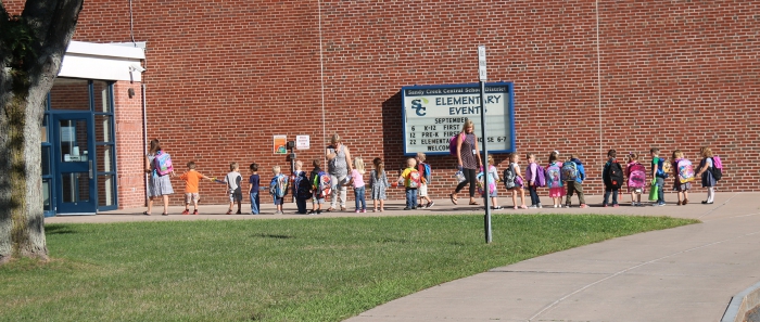Students line up after exiting the bus and walk together with their teachers to their classroom on the first day of classes for the pre-kindergarten class.