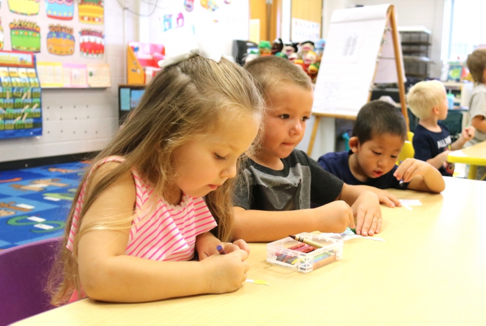 Pre-kindergarten students color their birthday cake to place on a display in the classroom.