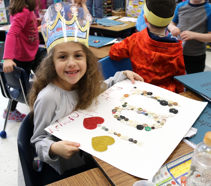 Burke Harvey proudly displays her 100 buttons poster she created to mark the 100th day of school. 