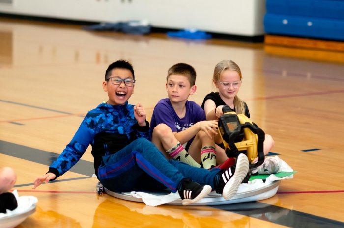 A team of fifth-graders race across the gymnasium on their hovercraft.