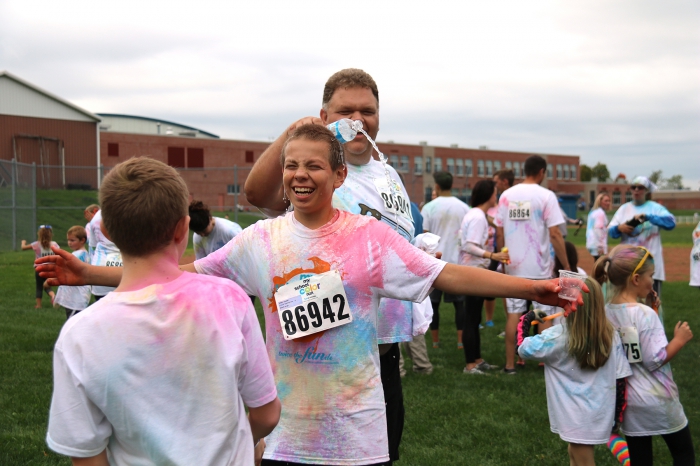 Nils Landis does a “payback” dousing to son, Alden, in response to the cup of water he had playfully dumped on his father seconds earlier. The two had just finished the Cross the Creek Color Run. Alden is a member of the cross country team at Sandy Creek.