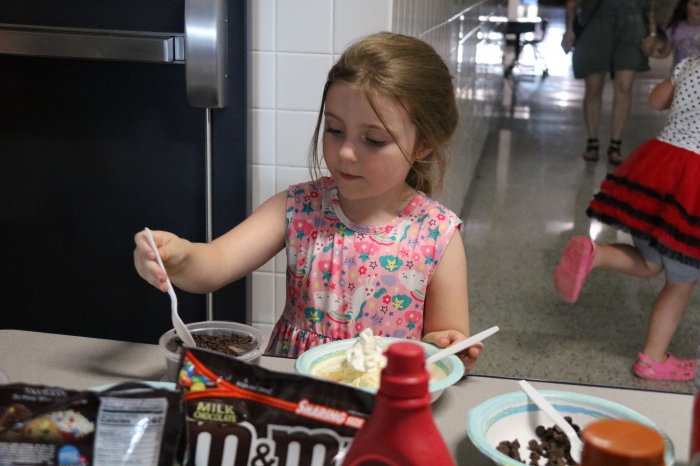 Kaywinnit Amyot adds chocolate sprinkles to her dish of ice cream  at the kindergarten ice cream social, Sundaes with Smiles.